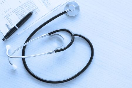 Black stethoscope on the table on blue background, top view and close up. Near is a pen and medical papersの写真素材