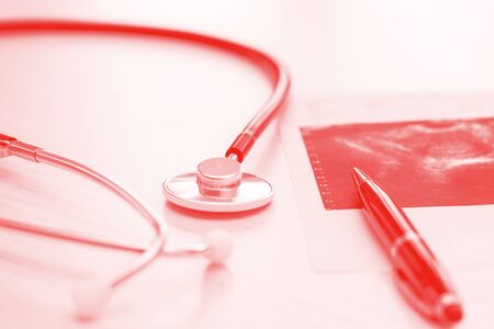 Doctor table on red backround with stethoscope, pen and fluorogram, close up. Horizontal imageの写真素材
