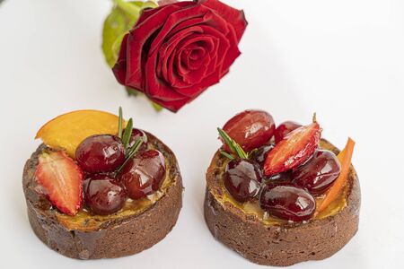 Two tasty chocolate cakes with icing fruits and berries on white background with red rose, isolated and macroの写真素材