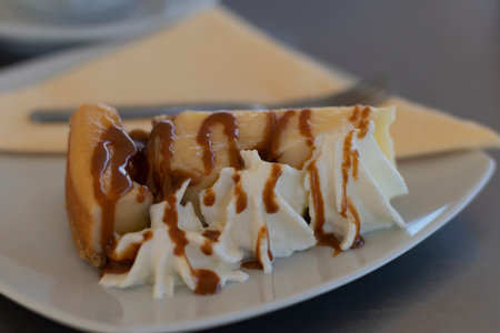 a piece of cheesecake topped with cream and caramel, served on a white plateの写真素材