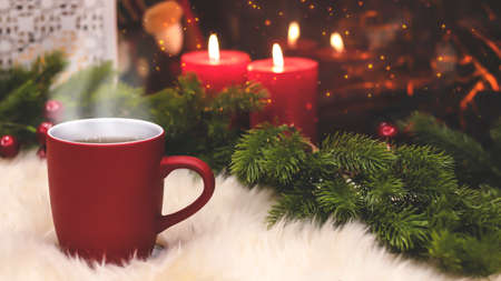 Red cup on the background of the New Year's interior, fireplace, candles, Christmas tree garland. Cozy winter evening by the fireplace. New Year and Christmas festive background.の写真素材