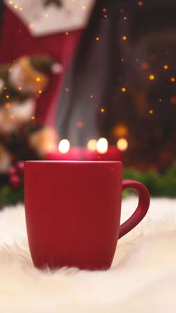 Red cup on the background of the New Years interior, fireplace, candles, Christmas tree garland. Cozy winter evening by the fireplace. New Year and Christmas festive background.の写真素材