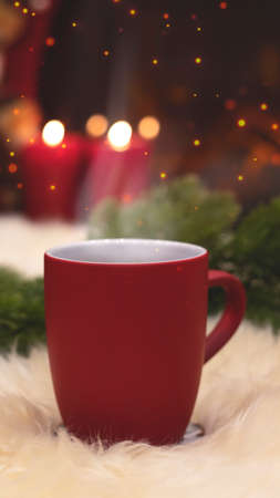 Red cup on the background of the New Years interior, fireplace, candles, Christmas tree garland. Cozy winter evening by the fireplace. New Year and Christmas festive background.の写真素材