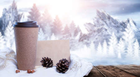 Hot coffee on a wooden table against the background of a winter landscape in a winter snowy forest. Coffee on the background of winter mountains. Snowflakes, frost.の写真素材