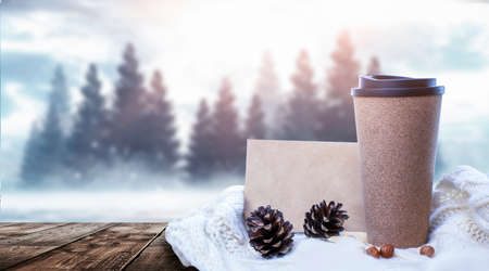 Hot coffee on a wooden table against the background of a winter landscape in a winter snowy forest. Coffee on the background of winter mountains. Snowflakes, frost.の写真素材