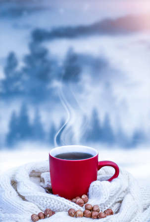 Red cup with coffee, tea on a snowy background, winter forest. A red cup against the background of a winter forest landscape on a soft, cozy scarf. Coffee, tea in the mountains.の写真素材