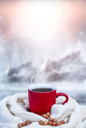 Red cup with coffee, tea on a snowy background, winter forest. A red cup against the background of a winter forest landscape on a soft, cozy scarf. Coffee, tea in the mountains.の写真素材