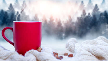 Red cup with coffee, tea on a snowy background, winter forest. A red cup against the background of a winter forest landscape on a soft, cozy scarf. Coffee, tea in the mountains.の写真素材