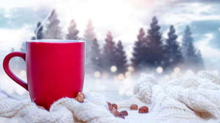 Red cup with coffee, tea on a snowy background, winter forest. A red cup against the background of a winter forest landscape on a soft, cozy scarf. Coffee, tea in the mountains.の写真素材