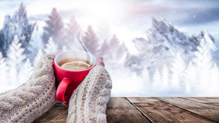 Red cup with coffee, tea in female hands on a snowy background, winter forest. A red cup in hands against the background of a winter forest landscape on soft, knitted sleeves. Coffee, tea on a woodenの写真素材