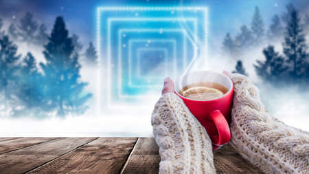 Red cup with coffee, tea in female hands on a snowy background, winter forest. A red cup in hands against the background of a winter forest landscape on soft, knitted sleeves. Coffee, tea on a woodenの写真素材