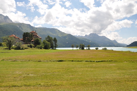 Grass field with a house and river with mountains in the backgroundの写真素材