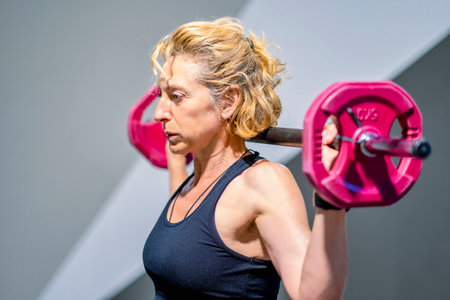 A woman is lifting a pink weight barbell. She is smiling and she is enjoying her workout. Fitness...