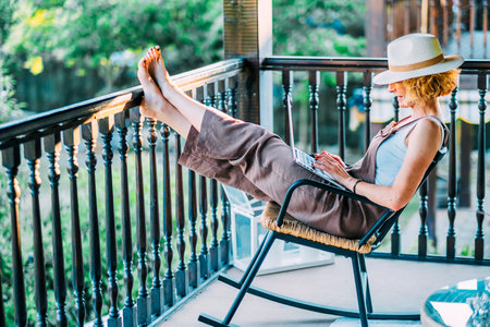 A woman is sitting on a rocking chair on a balcony, wearing a straw hatの写真素材