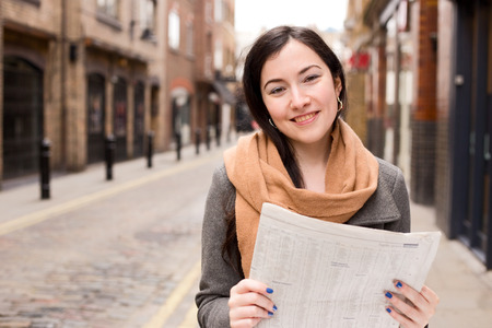 young woman reading a newspaper in the streetの写真素材