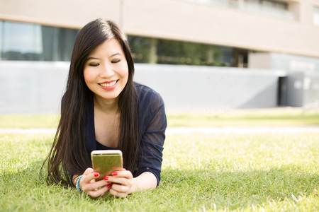 Japanese girl lying on grass sending a text messageの写真素材