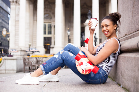 young woman in the street enjoying a coffee with her skateboardの写真素材