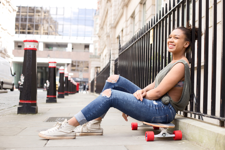 a young woman sitting on her skateboard in the streetの写真素材