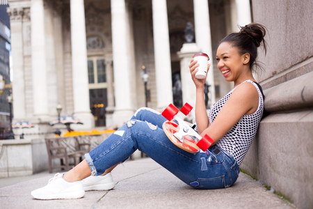 young woman in the street enjoying a coffee with her skateboardの写真素材