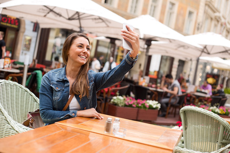 Young woman taking a selfie sitting outside a restaurantの写真素材