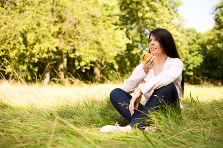young woman sitting in the park holding some fruitの写真素材