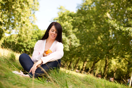 young woman sitting in the park holding an orangeの写真素材