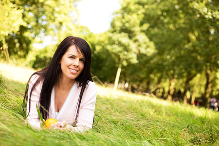 young woman lying in the grass holding an orangeの写真素材