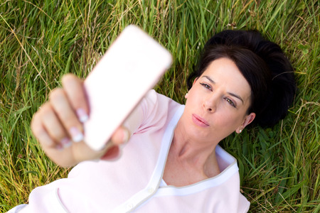 woman lying on the grass taking a selfieの写真素材