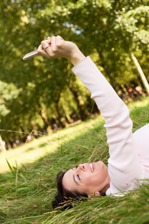 young woman lying on the grass taking a selfieの写真素材