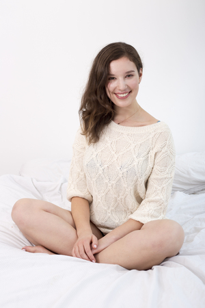 Happy young woman sitting on her bedの写真素材