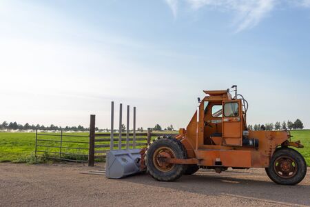Side angle of orange tractor with a plow in a field with blue sky in the backgroundの写真素材
