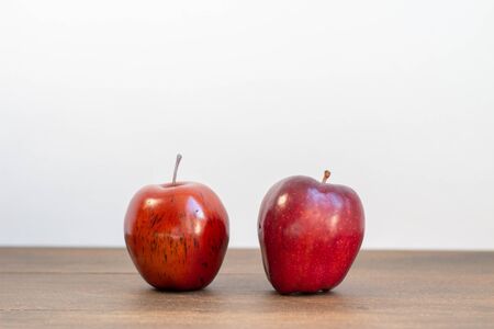 A fake red delicious and real apple next to each other on a white backgroundの写真素材