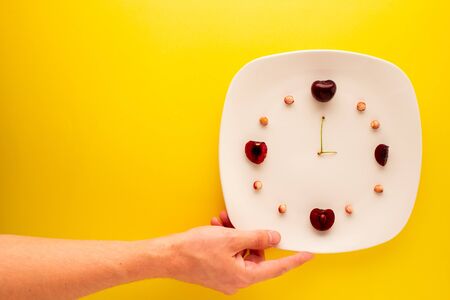 Hand reaching for a plate with leftover cherries showing the time.