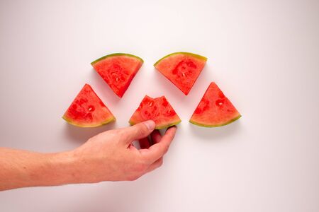 Person reaching for a bitten slice of watermelon against a white background.