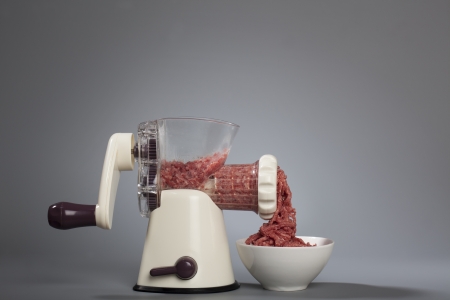 Household meat grinder with some minced meat coming out into a bowl.