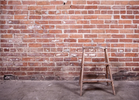 Small wooden ladder standing empty in front of a red-brick wall Slight sepia-toned and vignetting の写真素材