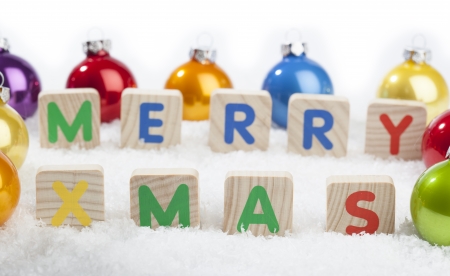 Merry Xmas text in front of Christmas decoration baubles in different colors on a (artificial) snow ground.の写真素材