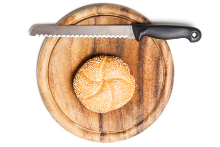 Bread roll covered with sesame seeds on cutting board with knife, typical German breakfast...
