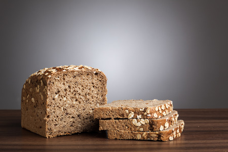 Loaf of wholemeal bread and slices on table in front of gray background.