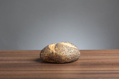 Single poppy seed bread roll on a wooden table 