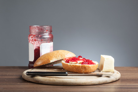 Breakfast plate with knife, bread roll with red rasberry jam and a piece of butter