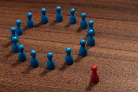 Left outside the circle. Concept with toy pawn figurines on wood table.