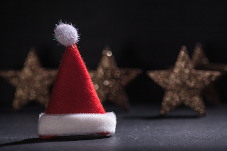 Red and white Santa Claus hat on a black underground, with glittering star background.の写真素材
