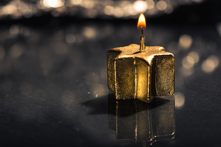 Lit golden advent candle, on a dark black slate underground, low key lighting, shallow depth of field.の写真素材