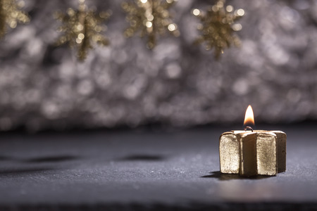 Lit golden advent candle, on a dark black slate underground, low key lighting, shallow depth of field, with star ornaments on top.の写真素材