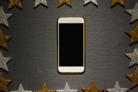 Smart phone, Christmas decoration frame on slate background with frame of golden and silver stars,...