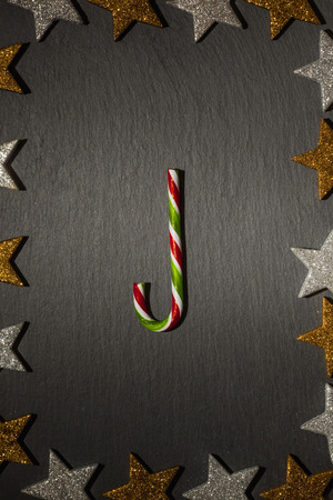 Red green striped candy cane on slate background with frame of golden and silver stars, Christmas decoration.の写真素材