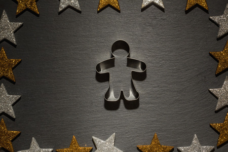 Cookie cutter for gingerbread man on slate background with frame of golden and silver stars, Christmas decoration.の写真素材