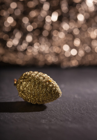 Golden Christmas tree ornament in form of a pine cone, with shallow depth of field in front of dark glitter bokeh backgroundの写真素材