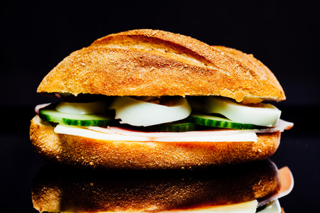Breakfast sandwich, potato bread roll with cucumber, ham and egg, chees, on black background with reflection.の写真素材